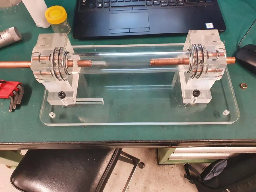 A machined clear acrylic fixture holding copper parts