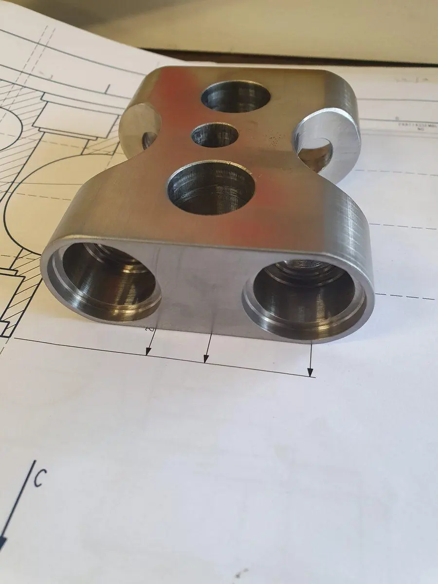 A machined stainless manifold block sitting on the drawing it was made from